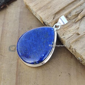 May include: A teardrop-shaped pendant featuring a deep blue lapis lazuli stone set in sterling silver. The stone has a sparkly, glittery texture.