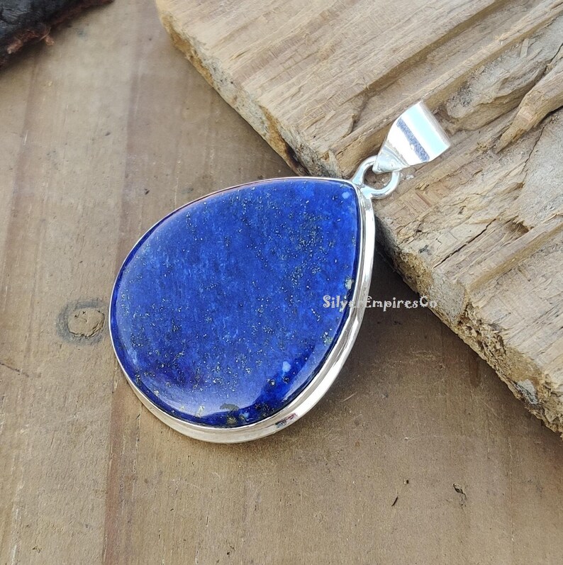 May include: A teardrop-shaped pendant featuring a deep blue lapis lazuli stone set in sterling silver. The stone has a sparkly, glittery texture.