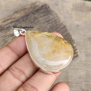 May include: A teardrop-shaped pendant with a clear quartz stone with gold inclusions. The pendant is made of sterling silver and has a bail for attaching to a chain.