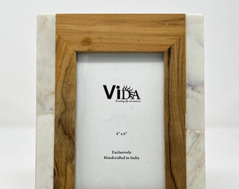 May include: A wooden picture frame with a white marble border. The frame is 4 inches by 6 inches and says "Exclusively Handcrafted in India".