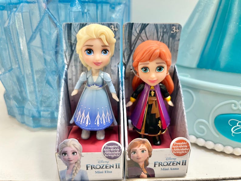 May include: Two Frozen II Mini dolls, Elsa and Anna, in their original packaging. Elsa wears a blue dress, and Anna wears a black and purple outfit. The packaging features character images and the text "Frozen II".