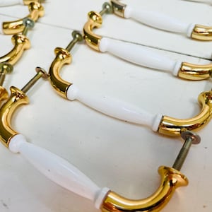 Puede incluir: Un juego de seis tiradores de puerta de armario de cerámica blanca y dorada. Los tiradores tienen un diseño simple y elegante con una forma curva y una manija de cerámica blanca.