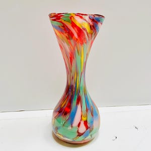 May include: A vibrant glass vase with a flared top and a rounded base. The vase is adorned with a swirl of red, yellow, blue, green, and pink hues. This decorative vase is a striking piece.