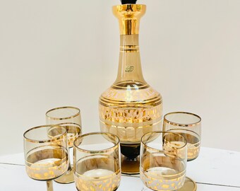 May include: A set of six brown glass decanter and glasses with gold accents. The decanter has a gold stopper and a white and gold design. The glasses have a gold rim and a white and gold design.