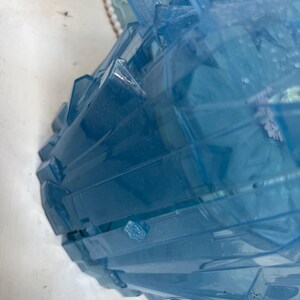 May include: A partially visible, light blue, plastic container with a geometric, faceted design. The container has a lid with a snowflake design. The container is on a white surface.