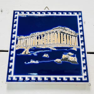Puede incluir: Un azulejo de cerámica azul y blanco con un borde blanco y un diseño de llave griega. El azulejo presenta una representación del Partenón en Atenas, Grecia.