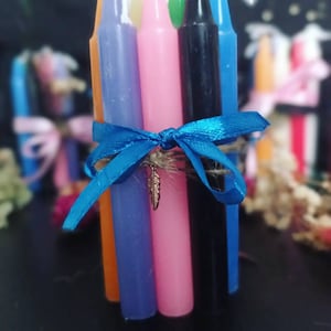 Peut inclure: Un lot de six bougies colorées liées ensemble avec un ruban bleu et un petit charme en forme de plume. Les bougies sont orange, bleu, rose, noir et bleu.