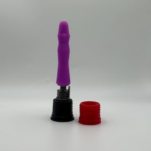 Puede incluir: Un objeto cilíndrico morado con una base negra y una tapa roja. El objeto tiene un mecanismo de resorte y está diseñado para encajar en un dispositivo más grande. La tapa roja es una pieza separada.