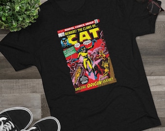 Può includere: Maglietta nera con una copertina di fumetto vintage che mostra una donna in una tuta da gatto gialla. La copertina recita "BEWARE! THE CLAWS OF... THE CAT" e "AMAZING ORIGIN ISSUE!"