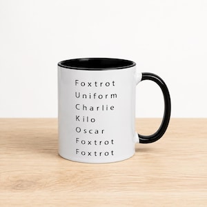 May include: A white ceramic mug with a black interior and a black handle. The exterior features black text printed in a vertical list using the NATO phonetic alphabet: Foxtrot, Uniform, Charlie, Kilo, Oscar, Foxtrot, Foxtrot, spelling out a phrase.
