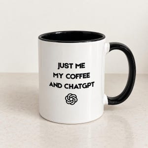 May include: A white ceramic mug with a black interior and a black handle. The front of the mug features the black text "JUST ME MY COFFEE AND CHATGPT" printed in a sans-serif font, positioned above a black circular ChatGPT logo icon.