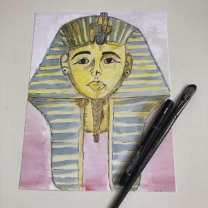 May include: A watercolour painting of a pharaoh's head wearing a golden headdress with blue and yellow accents. The background is a soft pink.