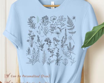 May include: Pale blue t-shirt with a black and white botanical print of flowers and plants. The shirt has rolled sleeves and a knotted hem. Text on the shirt says "Can Be Personalized (Free)", "Back Side Printing Possible", and "Multiple Colors Available".