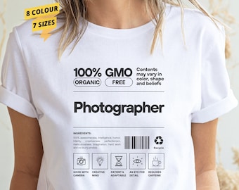 May include: White t-shirt with a black graphic that says "100% GMO (Organic) Free" and "Photographer". The graphic also includes a list of ingredients for a photographer, including a good camera, a creative mind, patience, an eye for detail, and caffeine.