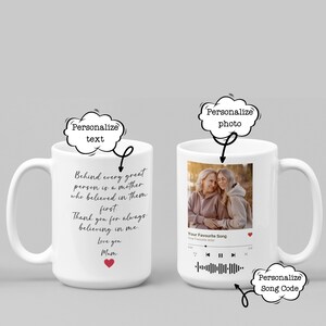 May include: White ceramic mug with a large handle, featuring a personalized design. One side has a photo and music player graphic, the other side has a heartfelt message: "Behind every great person is a mother... Love you, Mum."