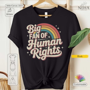 Könnte beinhalten: Ein schwarzes kurzärmeliges T-Shirt mit einem Grafikdesign und dem Text Big Fan Of Human Rights in einer Retro-Schriftart. Das Design enthält einen mehrfarbigen Regenbogenbogen in Rot-, Gelb- und Blautönen, akzentuiert durch kleine weiße Sternsymbole.