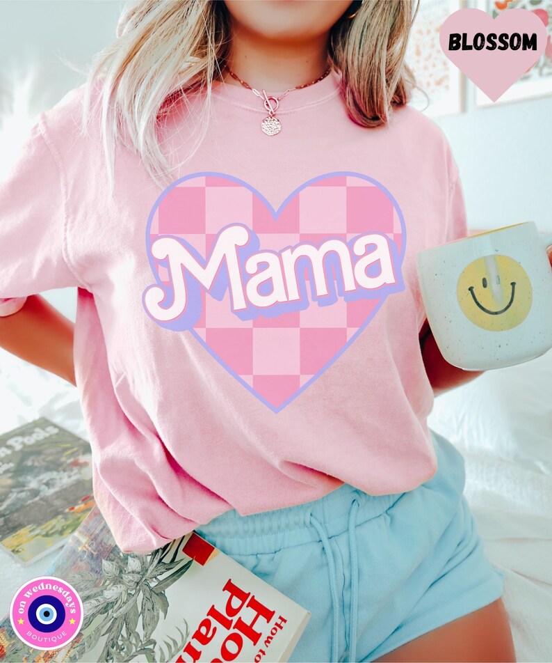 Puede incluir: Camiseta rosa con un coraz&oacute;n a cuadros y la palabra "Mama" en una fuente retro.