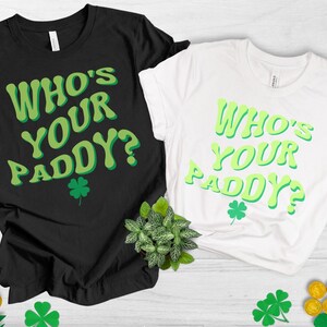 May include: Two t-shirts with the text "Who's Your Paddy?" in a green and white retro font. The shirts are black and white and have a shamrock design.