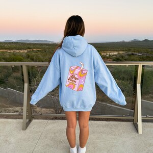 May include: A light blue hoodie with a graphic of a pink juice box on the back. The juice box has a straw and says "Fresh Boys Tears Gluten Free" on it.