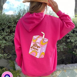 May include: Pink hoodie with a graphic of a cartoon juice box that says "Fresh Boys Tears Gluten-Free" on it.