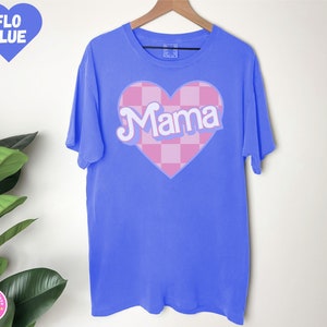 Puede incluir: Una camiseta azul con un coraz&oacute;n rosa a cuadros que dice "Mama" en letras blancas.