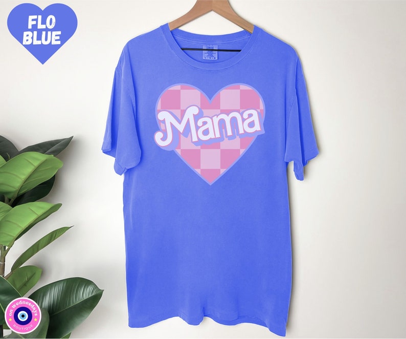 Puede incluir: Una camiseta azul con un coraz&oacute;n rosa a cuadros que dice "Mama" en letras blancas.