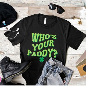 May include: Black t-shirt with a green graphic that says "Who's Your Paddy?" with a green four-leaf clover.