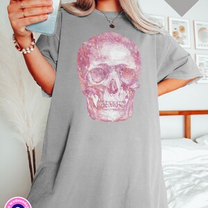 Op de afbeelding: Een grijs oversized T-shirt met een roze glitter schedel print. De schedel is een gedetailleerde anatomische illustratie.
