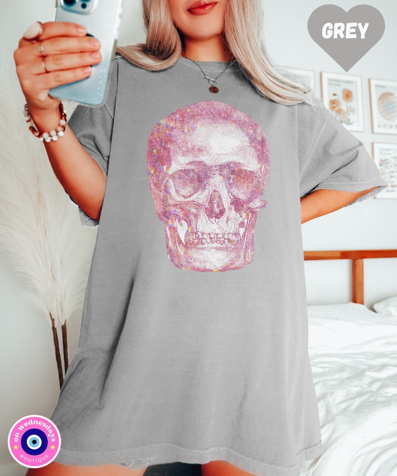 Op de afbeelding: Een grijs oversized T-shirt met een roze glitter schedel print. De schedel is een gedetailleerde anatomische illustratie.