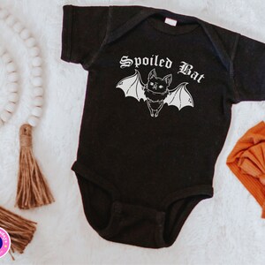 May include: Black baby onesie with a white graphic of a bat with the text "Spoiled Bat" in a gothic font.