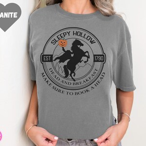 May include: Gray t-shirt with a black and white graphic of a headless horseman riding a horse. The graphic is a circle with the text "Sleepy Hollow" at the top, "Est 1790" at the bottom right, and "Dead and Breakfast Make Sure to Book a Head" around the outside.