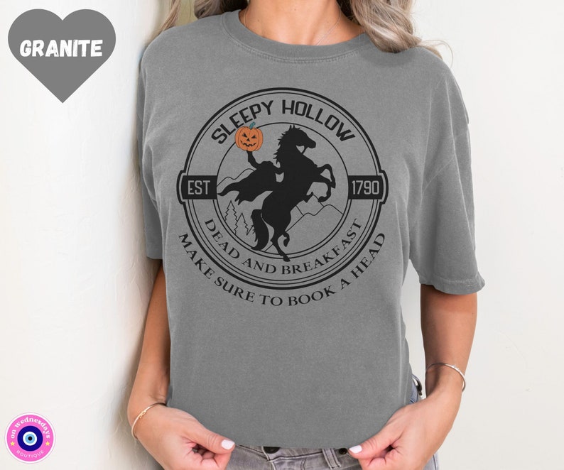 May include: Gray t-shirt with a black and white graphic of a headless horseman riding a horse. The graphic is a circle with the text "Sleepy Hollow" at the top, "Est 1790" at the bottom right, and "Dead and Breakfast Make Sure to Book a Head" around the outside.