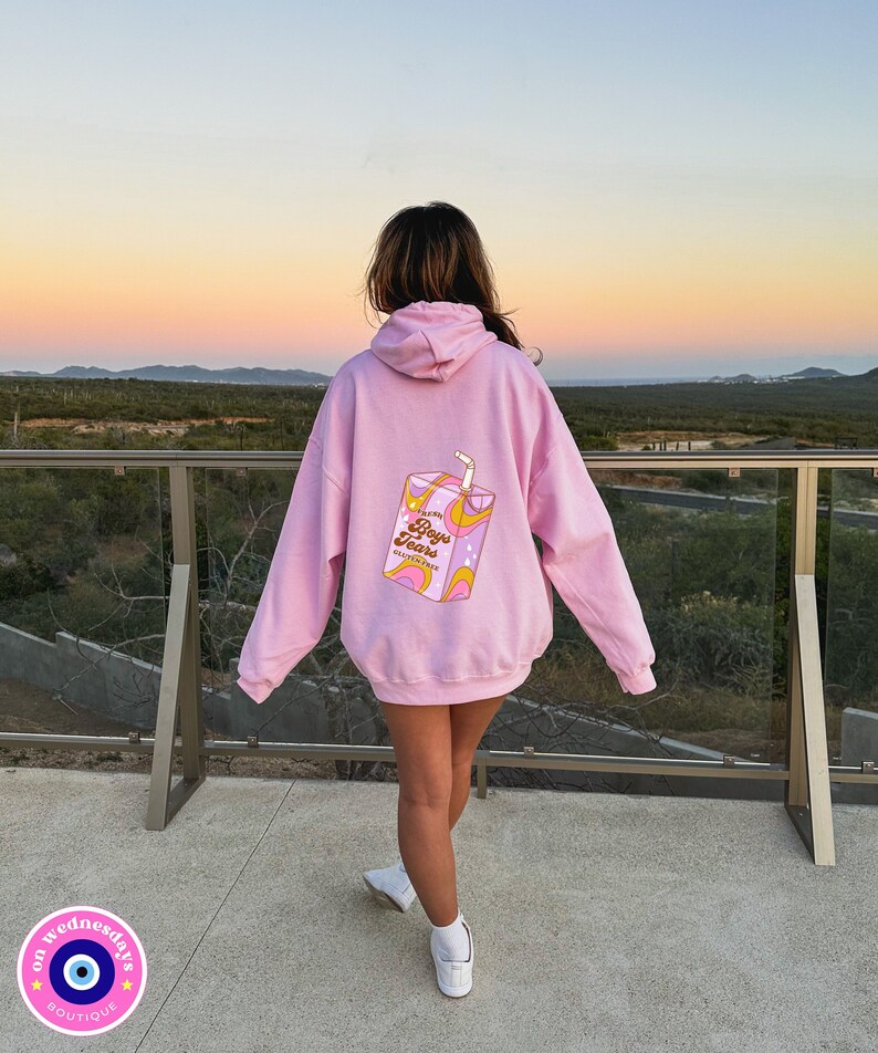 May include: Pink hoodie with a graphic of a juice box that says "Boys Tears" on the back. The hoodie is oversized and has a drawstring hood.