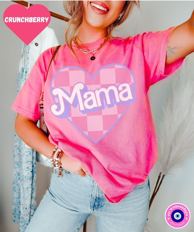 Puede incluir: Camiseta rosa con un coraz&oacute;n a cuadros y la palabra "Mama" en una fuente retro.