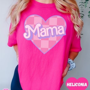 Puede incluir: Camiseta rosa con un gran gr&aacute;fico de coraz&oacute;n rosa y morado que dice "Mama" en una fuente retro. El coraz&oacute;n tiene un patr&oacute;n a cuadros.