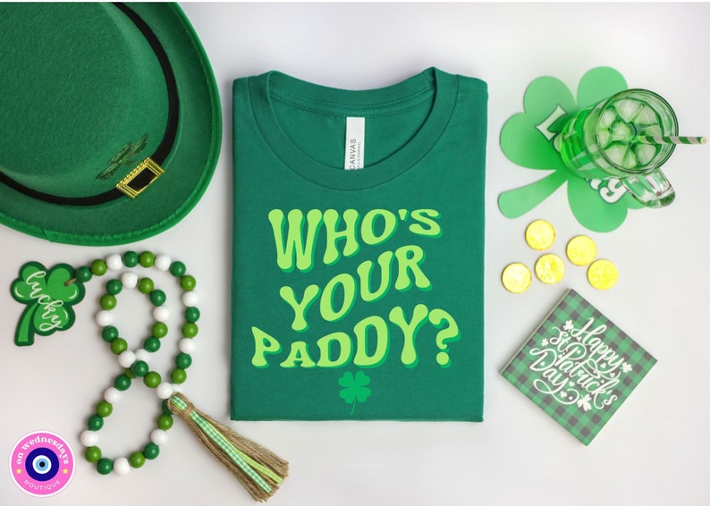 May include: Green t-shirt with the text "Who's Your Paddy?" in a retro font. The shirt is surrounded by St. Patrick's Day themed items, including a green hat, shamrocks, and gold coins.