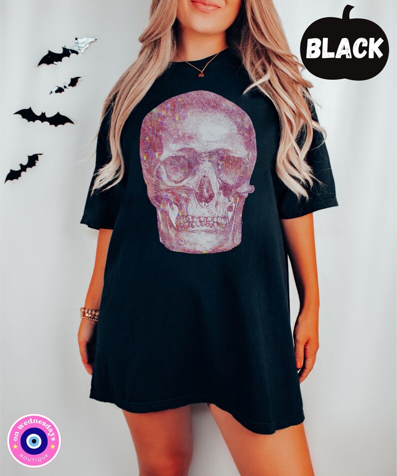 Op de afbeelding: Zwart oversized T-shirt met een glinsterende roze en witte schedelprint. De schedel heeft een gedetailleerd ontwerp met zichtbare tanden en oogkassen.