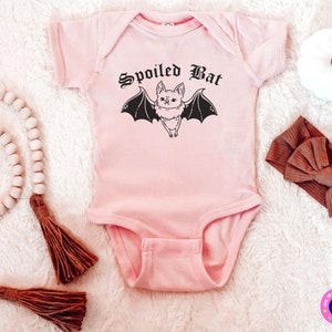 May include: Pink baby onesie with a black graphic of a bat with the text "Spoiled Bat" in a gothic font.