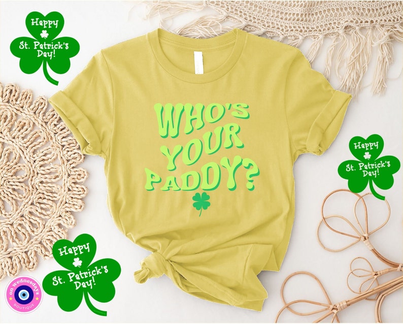 May include: Yellow t-shirt with the text "WHO'S YOUR PADDY?" in green letters. The shirt has a shamrock design and is surrounded by shamrock-shaped decorations with the text "Happy St. Patrick's Day!"