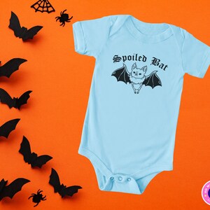 May include: A light blue baby onesie with a black bat graphic and the text "Spoiled Bat" in a gothic font.
