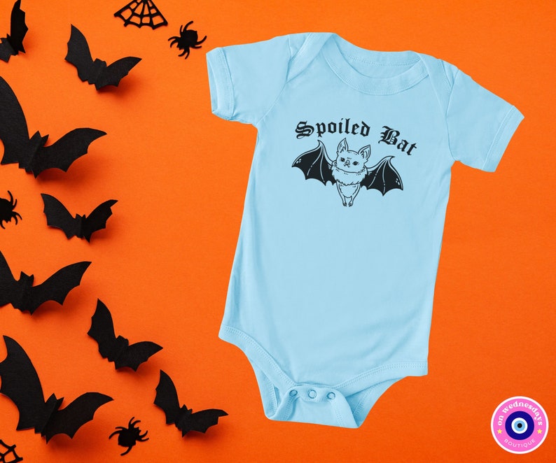 May include: A light blue baby onesie with a black bat graphic and the text "Spoiled Bat" in a gothic font.