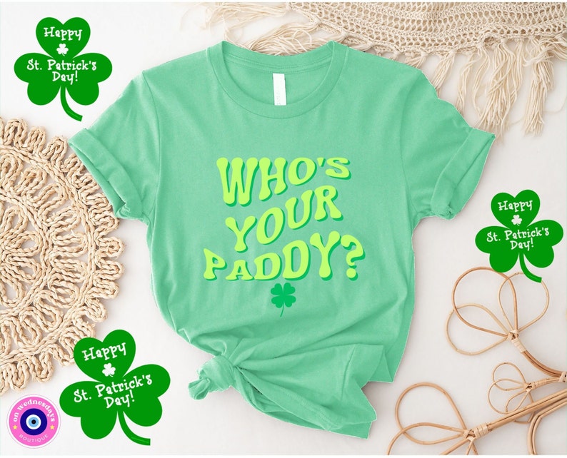 May include: A green t-shirt with the text "WHO'S YOUR PADDY?" in yellow letters. The shirt has a shamrock design on the front. There are three shamrock-shaped stickers with the text "Happy St. Patrick's Day!" around the shirt.
