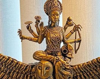May include: A gold-colored statue of a deity with multiple arms, riding an owl with outstretched wings. The deity is adorned with intricate details and jewelry.