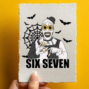 May include: A white card featuring a horror-themed clown illustration with sunflower eyes, a spiderweb, and bats. The text "SIX SEVEN" is at the bottom. The card is held against a yellow background.