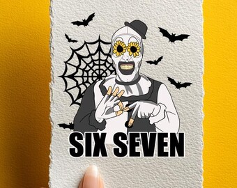Könnte beinhalten: Eine weiße Karte mit einer Horror-Illustration, die einen Clown mit Sonnenblumenaugen, einem Spinnennetz und Fledermäusen zeigt. Der Text "SIX SEVEN" befindet sich unten. Die Karte wird vor einem gelben Hintergrund gehalten.