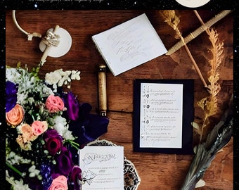 May include: A wedding planner with the title "The Ultimate Witchy Wedding Planner" and the text "To Manifest Your Most Magical of Days!"  The planner is surrounded by a bouquet of flowers, a wooden table, and a moon with stars in the background.