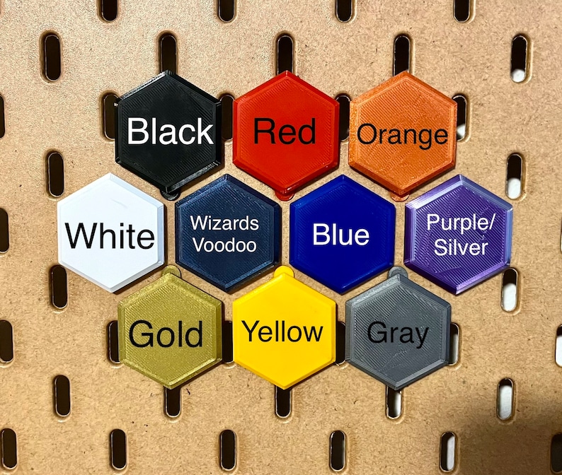 May include: A set of 10 hexagonal tiles in various colors, including black, red, orange, white, blue, purple, gold, yellow, and gray. Each tile has a different color and a word printed on it.