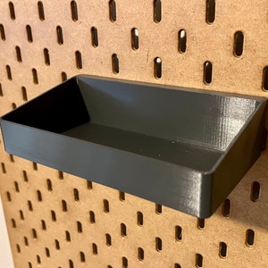 May include: A black plastic storage tray with a slightly angled front edge. The tray is mounted on a pegboard wall.