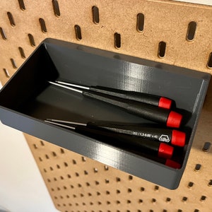 May include: A gray plastic tool organizer with four screwdrivers inside. The organizer is mounted on a pegboard wall.