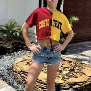 May include: A woman wearing a red and yellow cropped t-shirt with the text "CUSTOM TEXT" on the front. She is wearing denim shorts and black high-top sneakers.